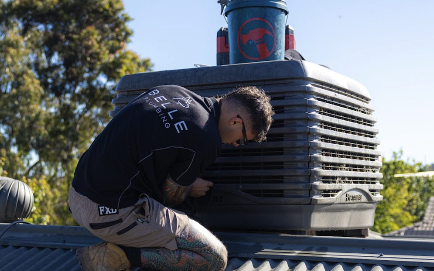 Belle Plumbing technician installing a new evaporative cooling system on a roof